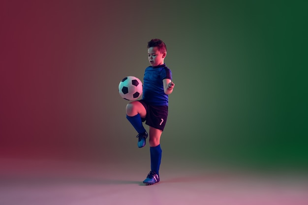 Teen male football or soccer player, boy on gradient background in neon light - motion, action, activity concept