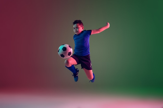 Teen male football or soccer player, boy on gradient background in neon light - motion, action, activity concept