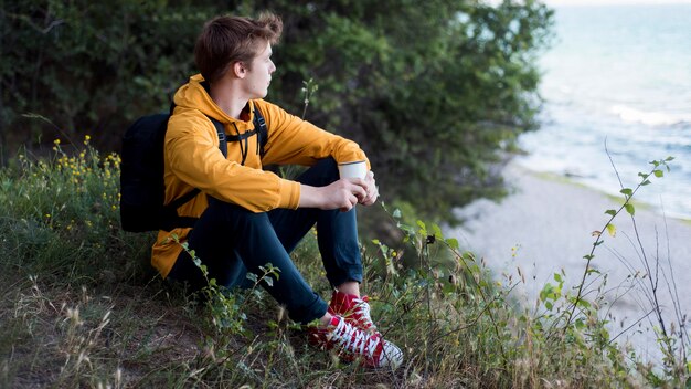 Teenager con zaino seduto a terra nella foresta