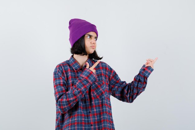 Teen woman in checked shirt and purple beanie pointing right looking focused