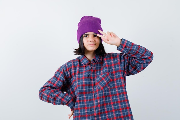Teen woman in checkered shirt and beanie gesticulating isolated