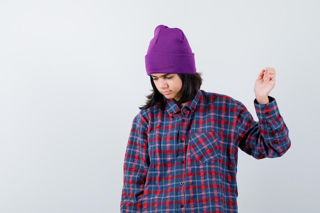 Teen woman in checkered shirt and beanie gesticulating isolated