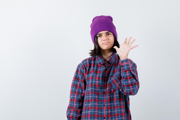 Teen woman in checkered shirt and beanie gesticulating isolated