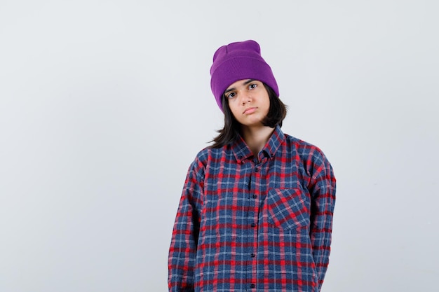 Teen woman in checkered shirt and beanie gesticulating isolated