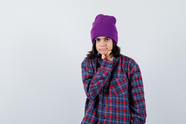 Teen woman in checkered shirt and beanie gesticulating isolated