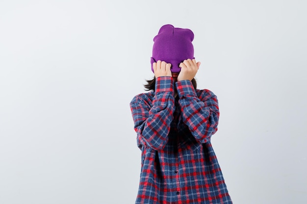 Teen woman in checkered shirt and beanie gesticulating isolated