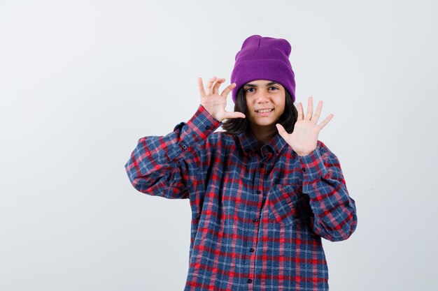 Teen woman in checkered shirt and beanie gesticulating isolated