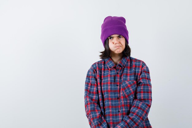 Teen woman in checkered shirt and beanie gesticulating isolated