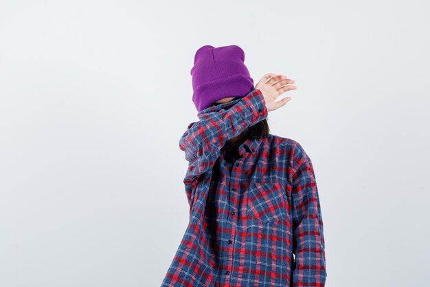 Teen woman in checkered shirt and beanie gesticulating isolated