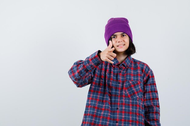 Teen woman in checkered shirt and beanie gesticulating isolated