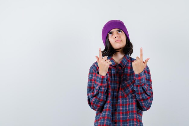 Teen woman in checkered shirt and beanie gesticulating isolated