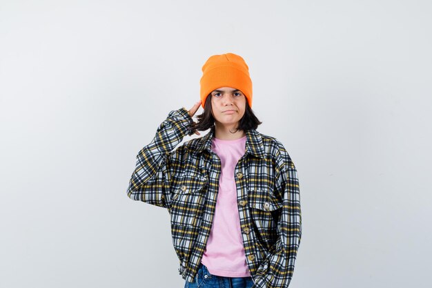 Teen woman in checkered shirt and beanie gesticulating isolated