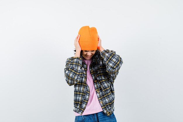 Teen woman in checkered shirt and beanie gesticulating isolated