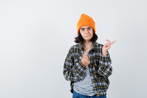 Teen woman in checkered shirt and beanie gesticulating isolated