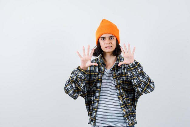 Teen woman in checkered shirt and beanie gesticulating isolated