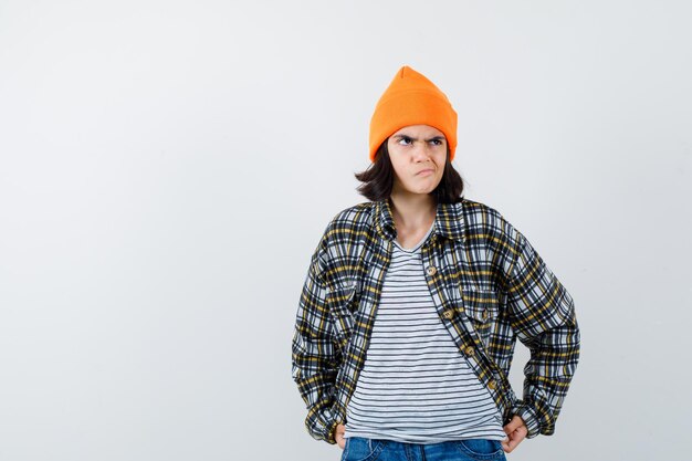 Teen woman in checkered shirt and beanie gesticulating isolated