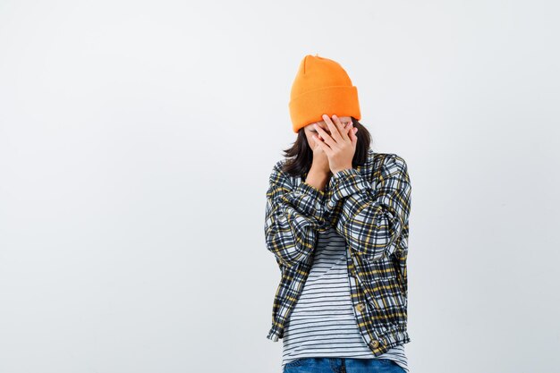 Teen woman in checkered shirt and beanie gesticulating isolated