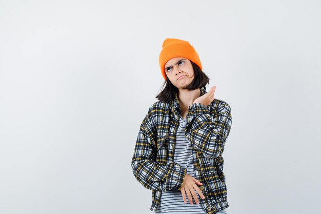 Teen woman in checkered shirt and beanie gesticulating isolated