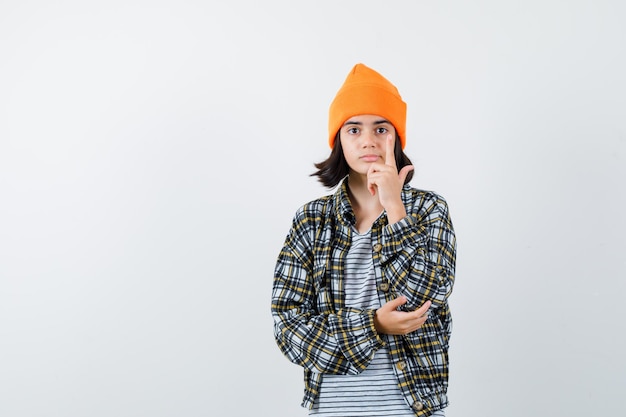 Teen woman in checkered shirt and beanie gesticulating isolated