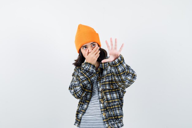 Teen woman in checkered shirt and beanie gesticulating isolated