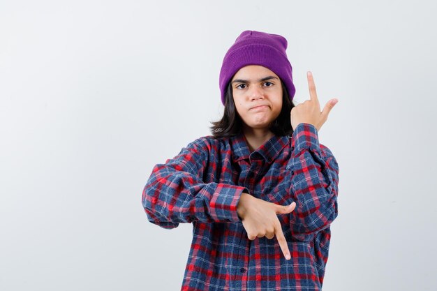 Teen woman in checkered shirt and beanie gesticulating isolated