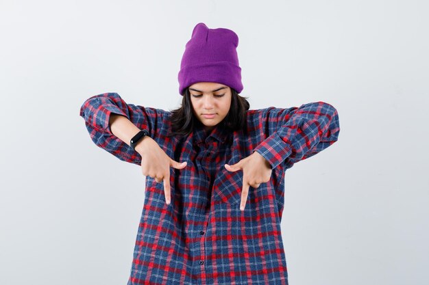 Teen woman in checkered shirt and beanie gesticulating isolated