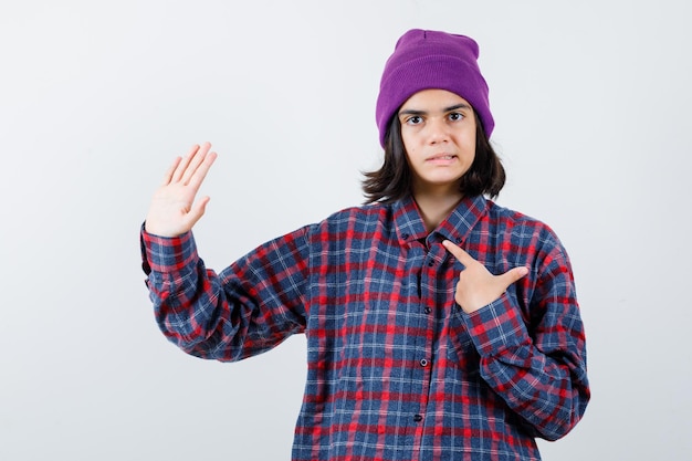 Teen woman in checkered shirt and beanie gesticulating isolated