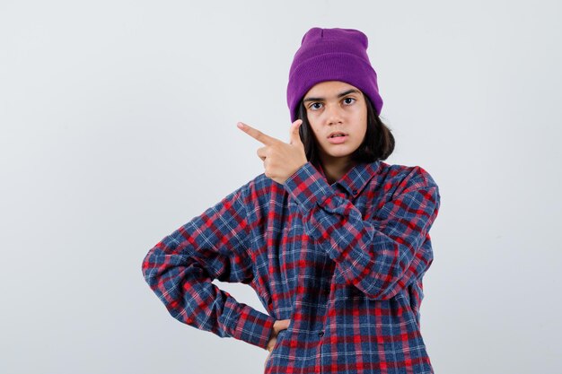 Teen woman in checkered shirt and beanie gesticulating isolated