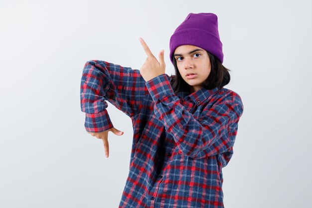 Teen woman in checkered shirt and beanie gesticulating isolated