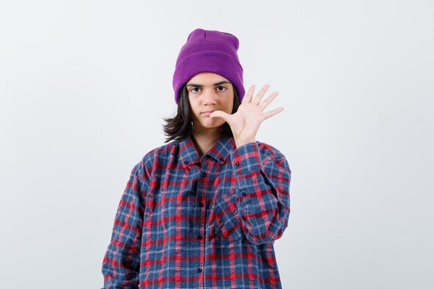 Teen woman in checkered shirt and beanie gesticulating isolated