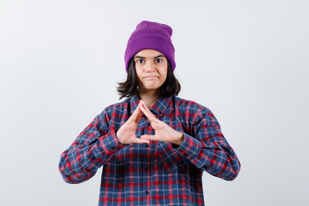 Teen woman in checkered shirt and beanie gesticulating isolated