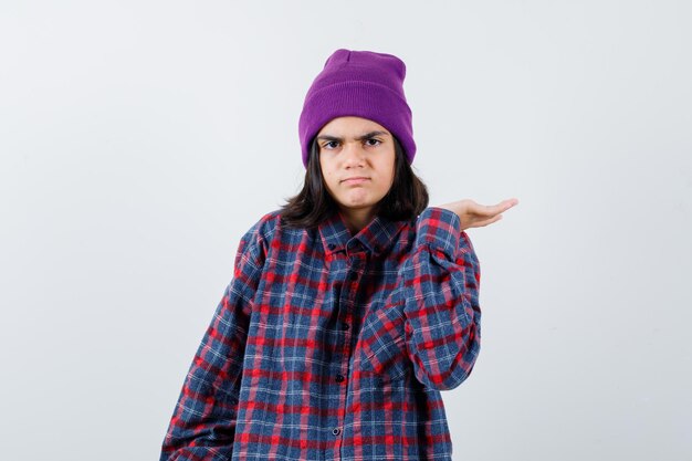 Teen woman in checkered shirt and beanie gesticulating isolated