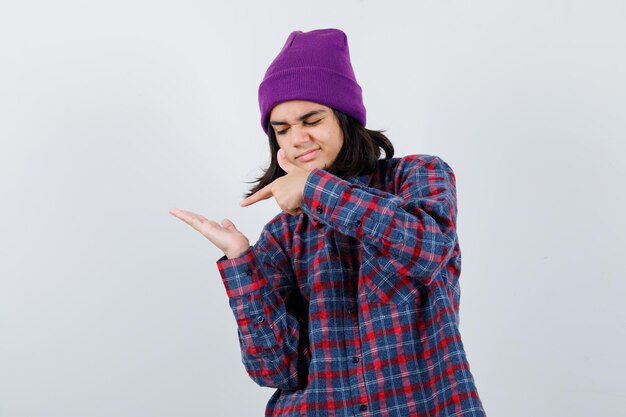 Teen woman in checkered shirt and beanie gesticulating isolated