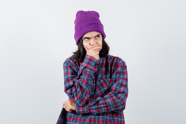 Teen woman in checkered shirt and beanie gesticulating isolated