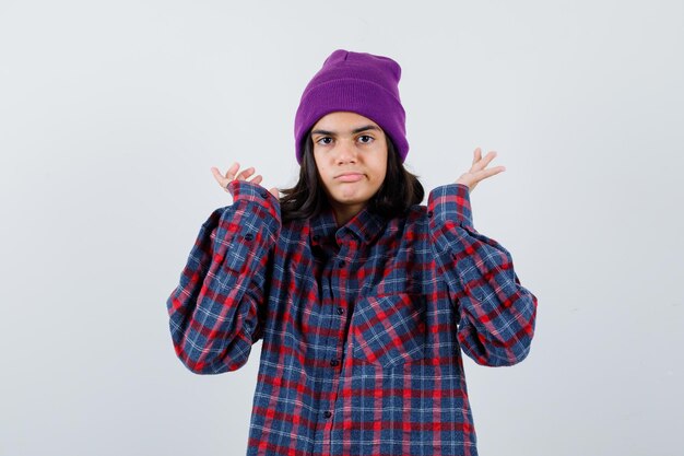 Teen woman in checkered shirt and beanie gesticulating isolated