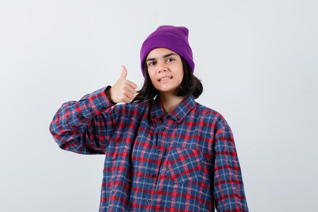 Teen woman in checkered shirt and beanie gesticulating isolated