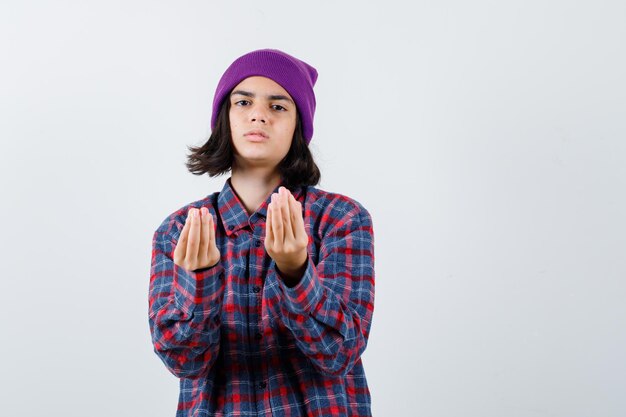 Teen woman in checkered shirt and beanie gesticulating isolated