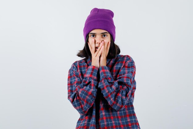 Teen woman in checkered shirt and beanie gesticulating isolated