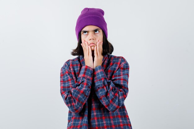 Teen woman in checkered shirt and beanie gesticulating isolated