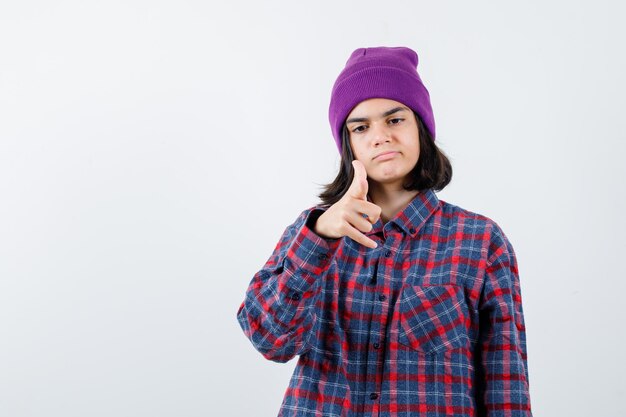 Teen woman in checkered shirt and beanie gesticulating isolated