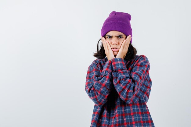 Teen woman in checkered shirt and beanie gesticulating isolated