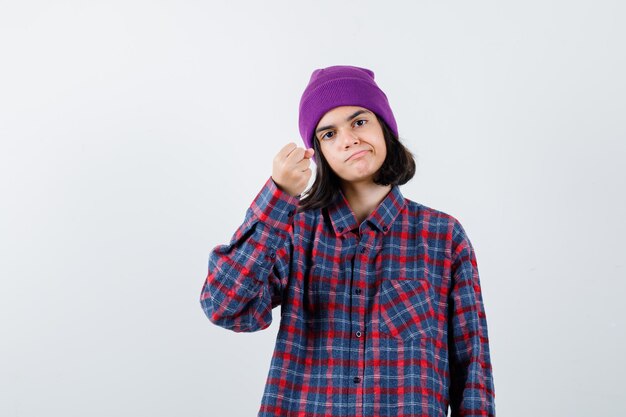 Teen woman clenching fist in checked shirt purple beanie looking cute 