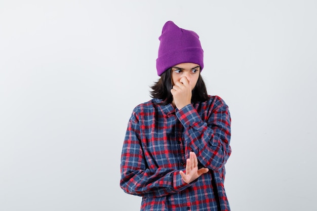 Teen woman covering mouth with hand showing stop sign in checked shirt looking serious