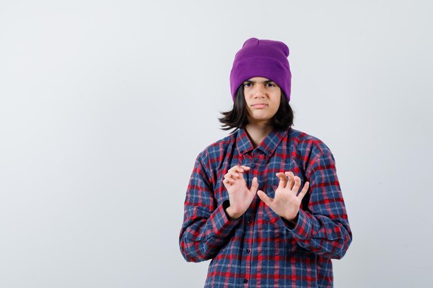 Teen woman keeping hands to defend herself in checkered shirt and beanie