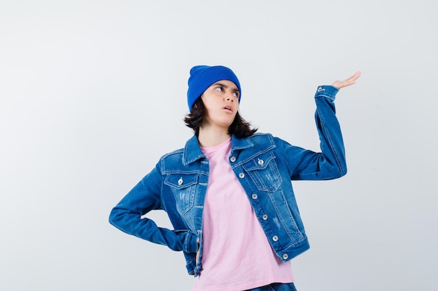 Teen woman in pink t-shirt and beanie holding hand on hip and stretching cupped hand