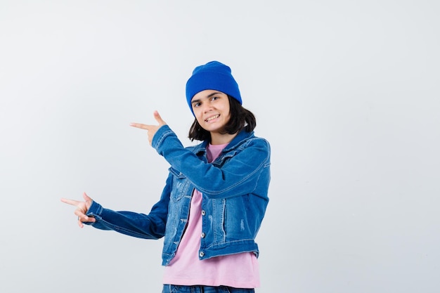 Teen woman pointing left with index fingers in pink t-shirt jean jacket looking cheery