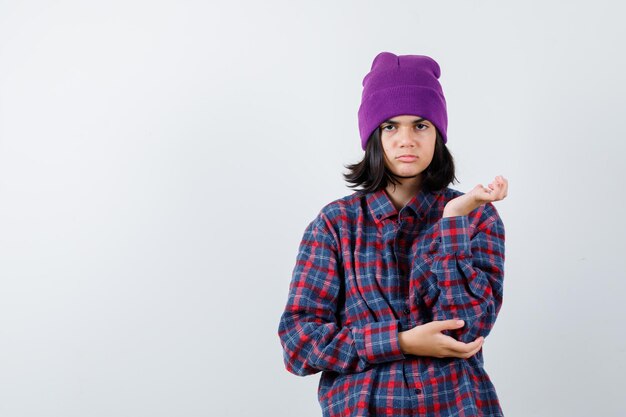 Teen woman raising hand in puzzled manner beanie looking confused