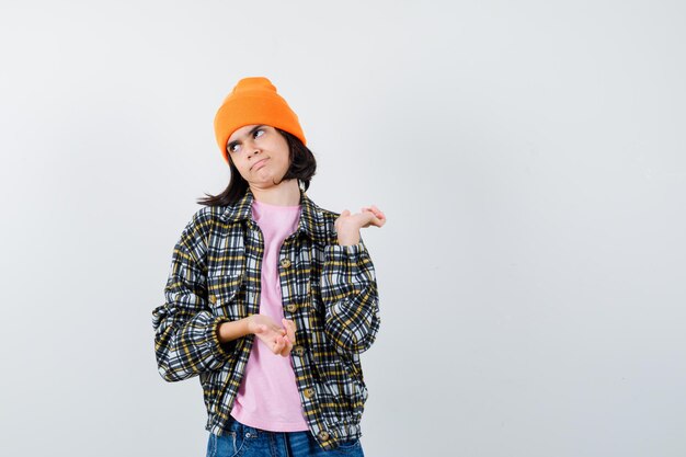 Teen woman spreading palms out in t-shirt jacket beanie looking confused