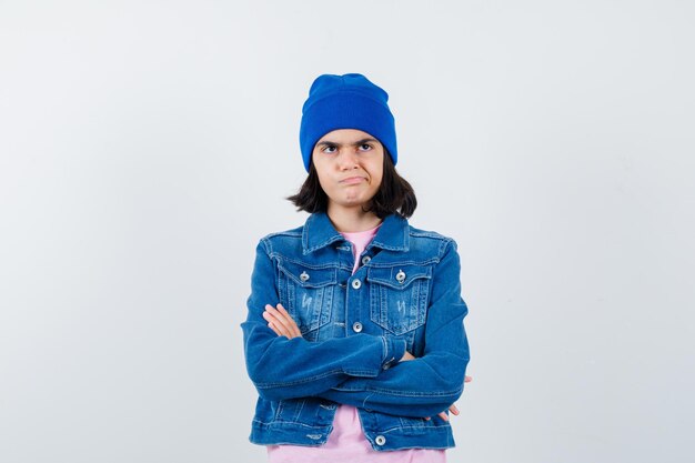 Teen woman standing arms crossed in pink t-shirt jean jacket beanie looking anxious