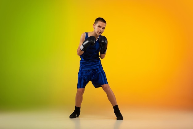 Free photo teenage boxer against gradient neon studio in motion of kicking, boxing